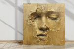 Serene human face emerging from cracked gold surface, warm gold and amber tones, dramatic mixed-media portrait canvas art
