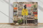 Standing figure in bright yellow jacket against collaged newspaper wall, bold mixed-media urban street art canvas print