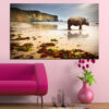 A rhino stands on sandy beach with ocean and sky behind it
