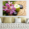 White orchid blooms rest beside a lit candle on dark wet stones, with bamboo stalks in soft focus behind
