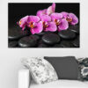 White orchid blooms rest beside smooth black spa stones on a dark reflective surface